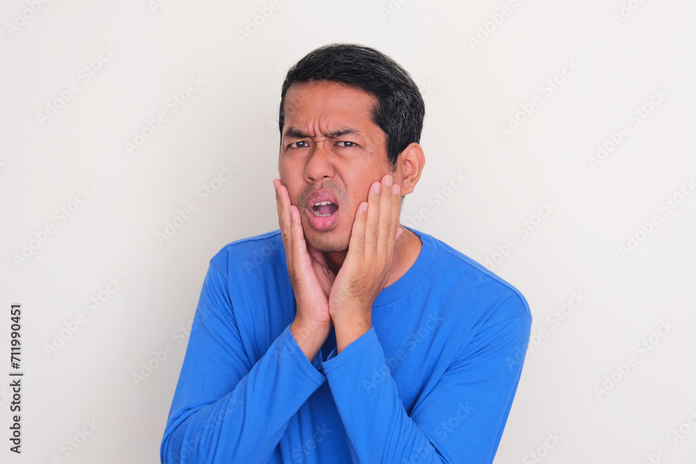 Adult Asian man touching his face with worry expression Adult Asian man touching his face with worry expression