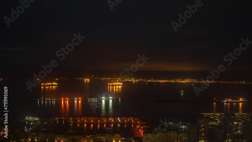 Night lights glowing on Gibraltar port, time lapse view. Vibrant cloudscape