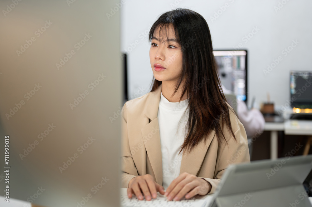 A focused Asian businesswoman is working on her tasks on her computer in the office. A focused Asian businesswoman is working on her tasks on her computer in the office.