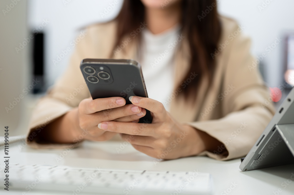 Cropped image of an Asian businesswoman using her phone, sending messages or chatting, at her desk Cropped image of an Asian businesswoman using her phone, sending messages or chatting, at her desk