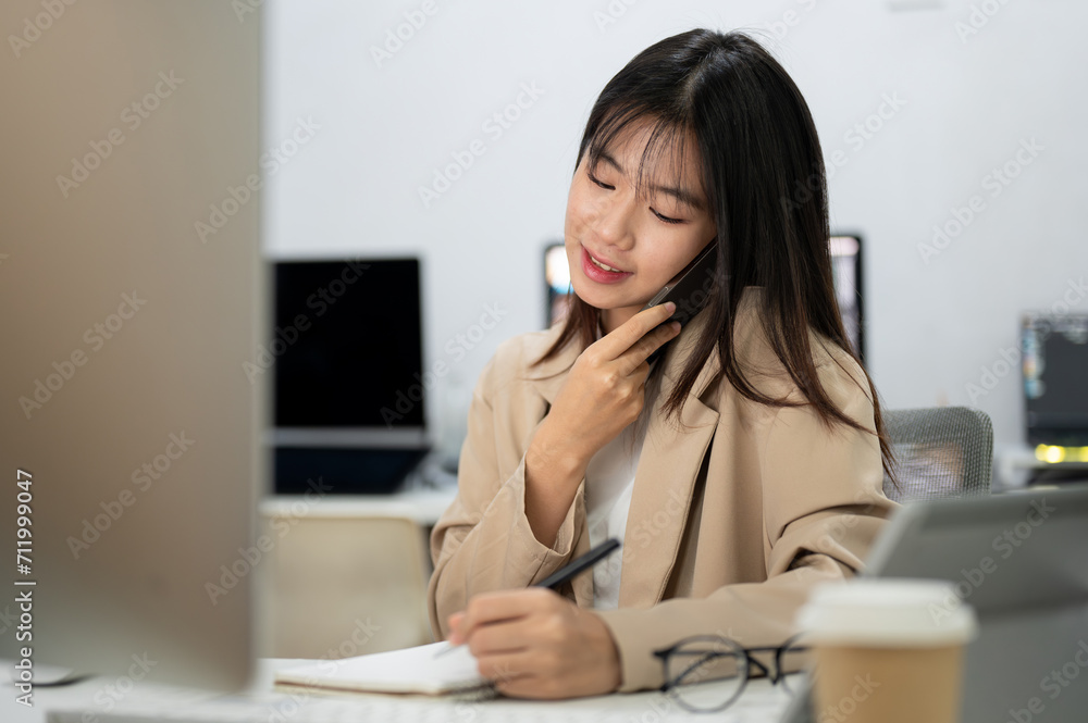 A young, beautiful Asian businesswoman is busy with her work in the office, talking on the phone. A young, beautiful Asian businesswoman is busy with her work in the office, talking on the phone.