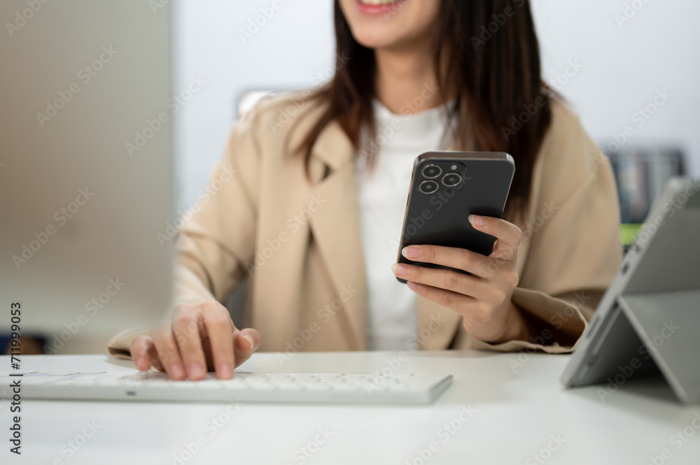 Cropped image of a businesswoman using her smartphone and typing on computer keyboard at her desk. Cropped image of a businesswoman using her smartphone and typing on computer keyboard at her desk.