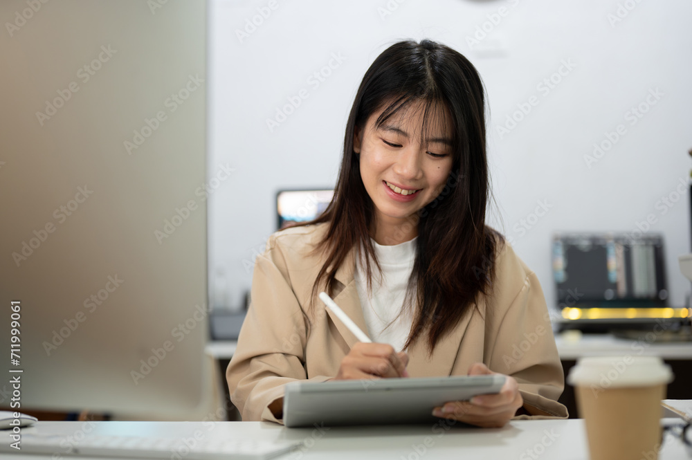 Attractive Asian businesswoman is working at her desk in the office, using her digital tablet. Attractive Asian businesswoman is working at her desk in the office, using her digital tablet.