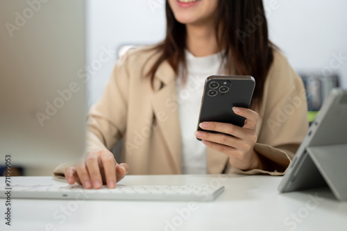 Cropped image of a businesswoman using her smartphone and typing on computer keyboard at her desk.