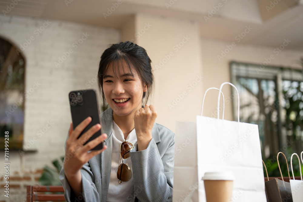 Young cheerful and pretty Asian woman is receiving a good news while sitting in a cafe. Young cheerful and pretty Asian woman is receiving a good news while sitting in a cafe.