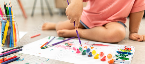 Happy moment little cute girl creating and water color painting activity with paint brushes on frame canvas at living room. Kids activity. Child physical, Emotional, Cognitive development concept. photo