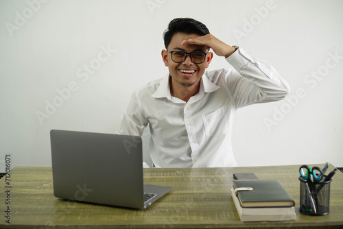 young asian businessman in a workplace looking far away with hand to look something wear white shirt with glasses isolated photo
