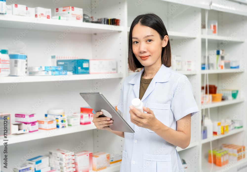 Beautiful asian woman pharmacist checks inventory of medicine in pharmacy drugstore. Professional Female Pharmacist wearing uniform standing near drugs shelves working with tablet. Beautiful asian woman pharmacist checks inventory of medicine in pharmacy drugstore. Professional Female Pharmacist wearing uniform standing near drugs shelves working with tablet.