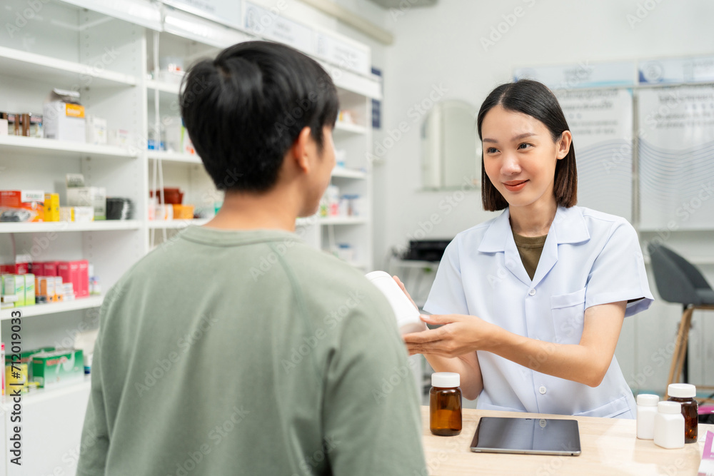 Fototapeta premium Pharmacist recommends medicines to customers.Taking the questions of medication. Asian female pharmacist giving prescription medications to customers at drugstore shelves.