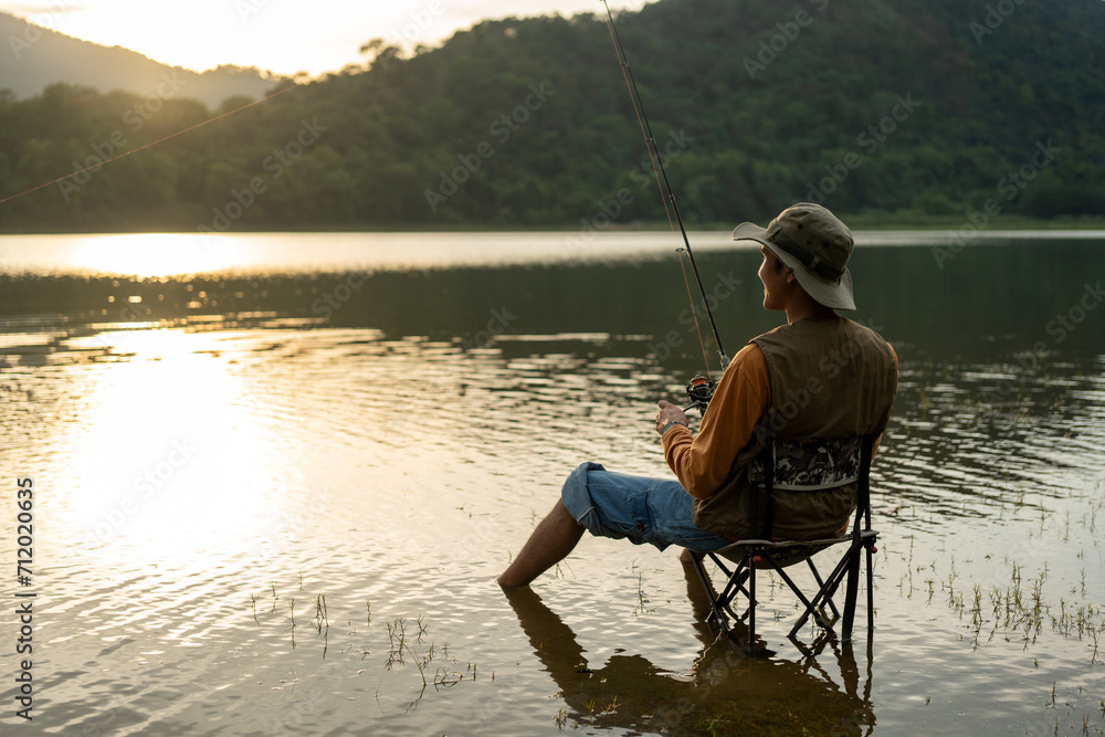 Enjoy moment of Handsome man fishing as a leisure activity during his vacation at the lake on sunset. Silhouette at sunset moment of man fishing rotation with reel. Enjoy moment of Handsome man fishing as a leisure activity during his vacation at the lake on sunset. Silhouette at sunset moment of man fishing rotation with reel.