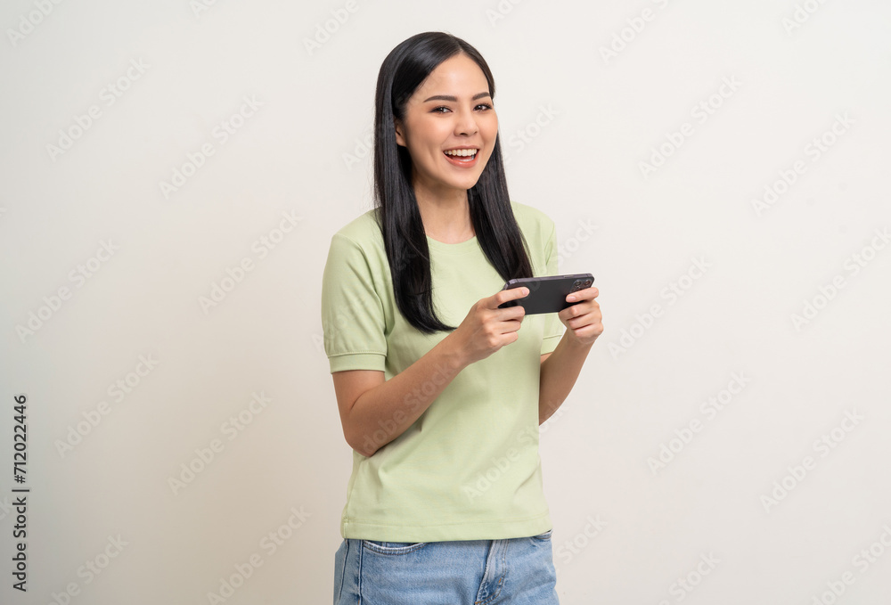 Excited Beautiful young asian women play mobile game and standing on isolated white background. Happy smiling female Playing game on smartphone winning victory moment. Very enjoy and fun relax time