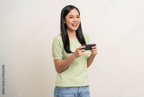 Excited Beautiful young asian women play mobile game and standing on isolated white background. Happy smiling female Playing game on smartphone winning victory moment. Very enjoy and fun relax time