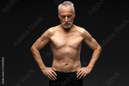 Senior retired man with gray hair shirtless with closed eyes standing isolated on black background