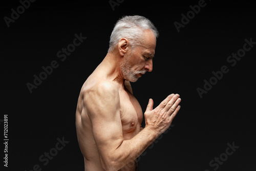 Side view portrait of serious strong man with naked torso gesturing, meditating, with eyes closed