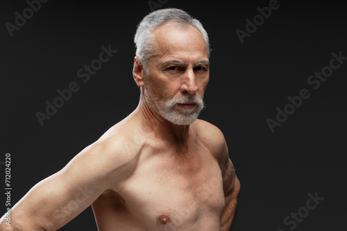 Portrait of attractive serious mature senior gray haired man with bare torso looking at camera