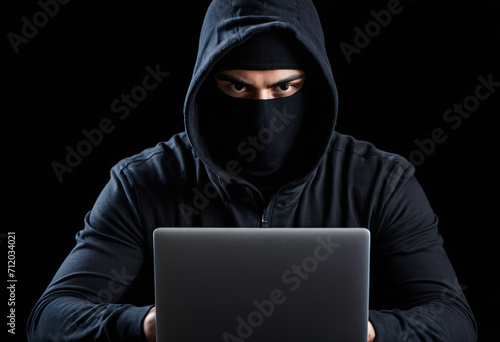 Hacker terrorist with balaclava mask, atack network from laptop over black background 