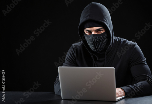 Hacker terrorist with balaclava mask, atack network from laptop over black background 