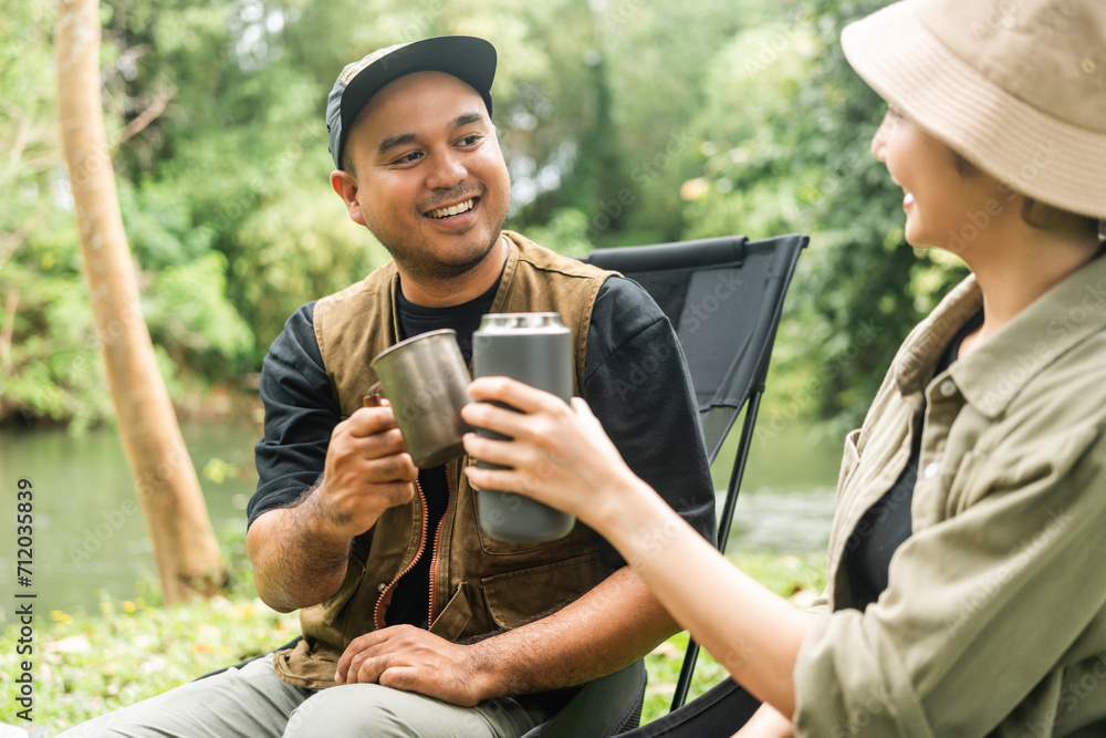 Young asian couple man and woman drinking coffee sitting in campsite outdoor. Two people camping in forest with coffee maker tools. Travel relax camping on vacation holiday weekend theme Young asian couple man and woman drinking coffee sitting in campsite outdoor. Two people camping in forest with coffee maker tools. Travel relax camping on vacation holiday weekend theme