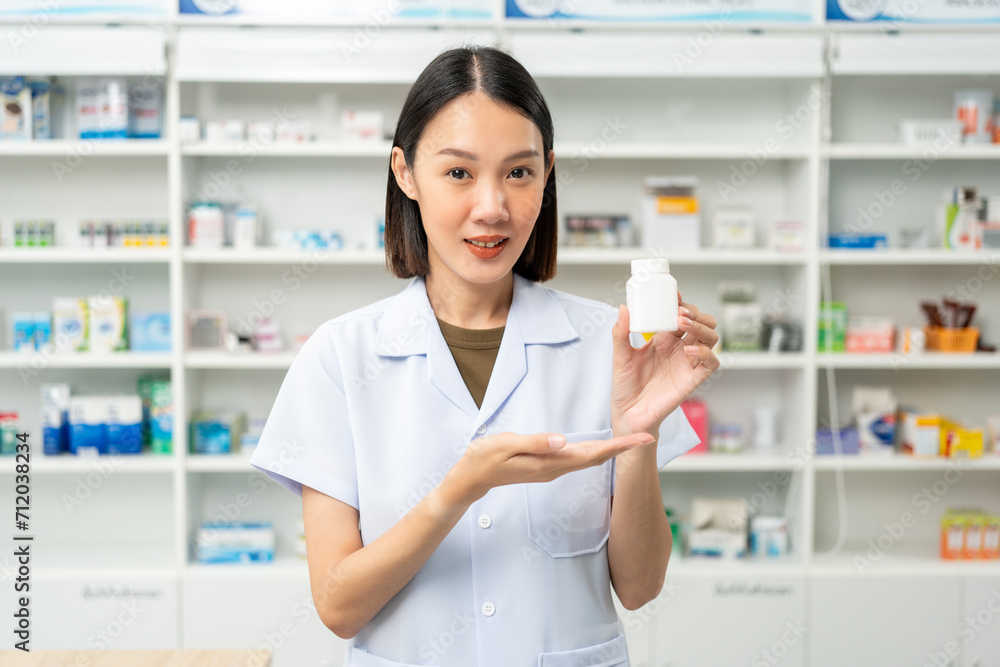 Professional Pharmacist woman in uniform holding medicine bottle near drug shelves counter. Pharmacist checks inventory of medicine in pharmacy drugstore. Professional Pharmacist woman in uniform holding medicine bottle near drug shelves counter. Pharmacist checks inventory of medicine in pharmacy drugstore.