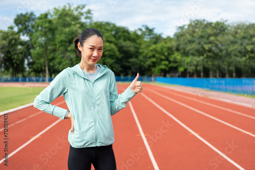 Attractive Young asian woman wearing sportswear running on track at sport stadium. Fit athlete female jogging outdoor standing pose. Exercise in the morning. Healthy and active lifestyle concept.