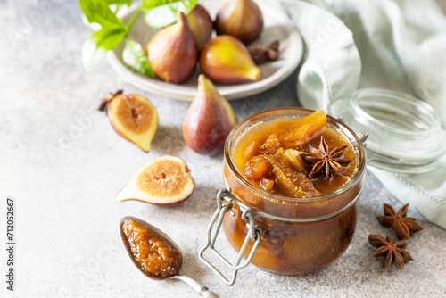 Homemade fig sweet jam in a glass jar with fresh figs on a light gray table. Autumn harvest preservation, healthy fermented food. Copy space.