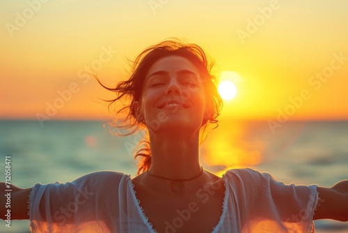 Happy woman with open arms and closed eyes on the seashore at sunset. photo