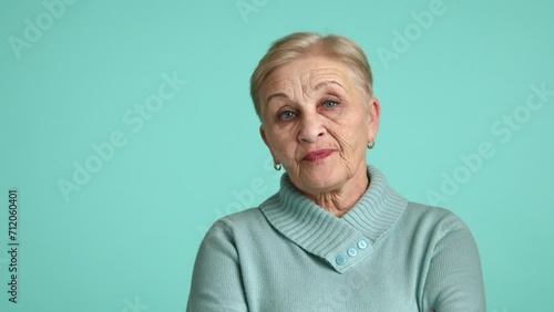 Serious elegant aged lady in blue sweater standing over blue background, crossing hands on chest, looking with distrust and disgust, expression of scorn. High quality 4k footage