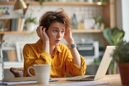 Angry freelance woman sitting with computer and macbook at table with confused and troubled expression photo