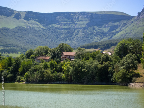 Fototapeta Naklejka Na Ścianę i Meble -  Panoramic view of the natural area of the Maroño reservoir in Alava on a sunny day with a high water level surrounded by trees, vegetation and mountains, in the background a small house.