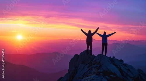 Two people silhouette with arms raised up on mountain top at sunset © MdKamrul
