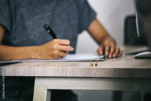 Wedding rings on wooden table with hand signing documents and judge gavel on the background. Marriage and divorce concept.