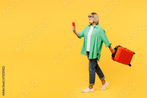 Traveler elderly woman wear green casual clothes hold mobile cell phone bag isolated on plain yellow background. Tourist travel abroad in free spare time rest getaway. Air flight trip journey concept.