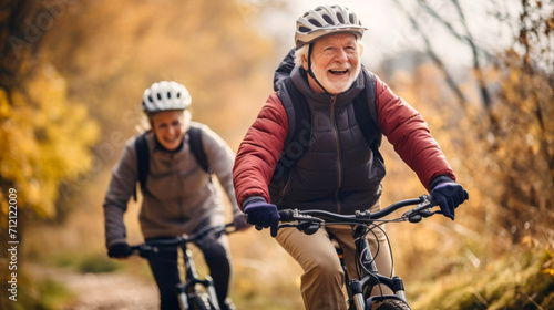 Elderly smiling man and woman, warmly dressed for fall in helmets, riding bicycles through a golden autumn forest. outdoor activities in the elderly. Healthy aging