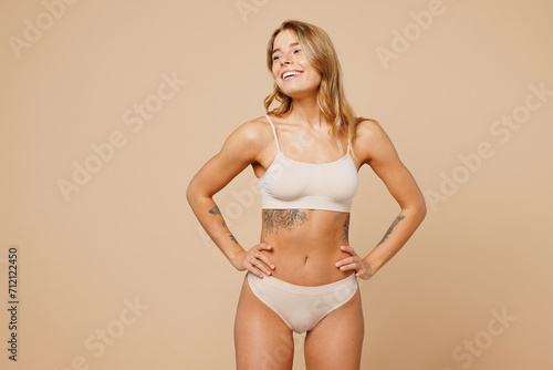 Young nice lady woman with slim body perfect skin wear nude top bra lingerie stand hold hands on waist looking aside on area isolated on plain pastel light beige background Lifestyle diet fit concept © ViDi Studio