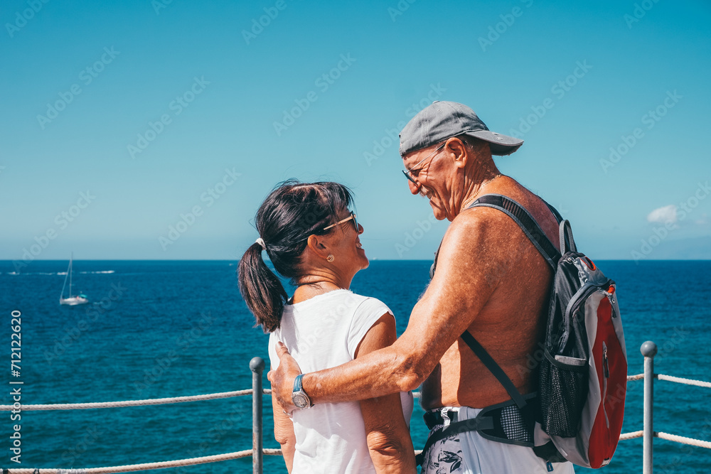 Back view of caucasian senior couple hugging looking into each other eyes outdoors in sea vacation. horizon over water. Elderly people enjoying healthy lifestyle  retirement and travel