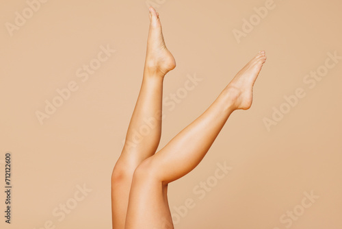 Close up cropped photo shot of raised up barefoot legs of woman with slim body perfect skin after shaving depilation procedure isolated on plain pastel beige background. Lifestyle diet fit concept. © ViDi Studio