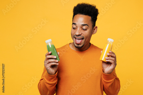 Young surprised man wear casual clothes hold show fruit juice green vegetable smoothie as detox diet isolated on plain yellow background. Proper nutrition healthy fast food unhealthy choice concept.