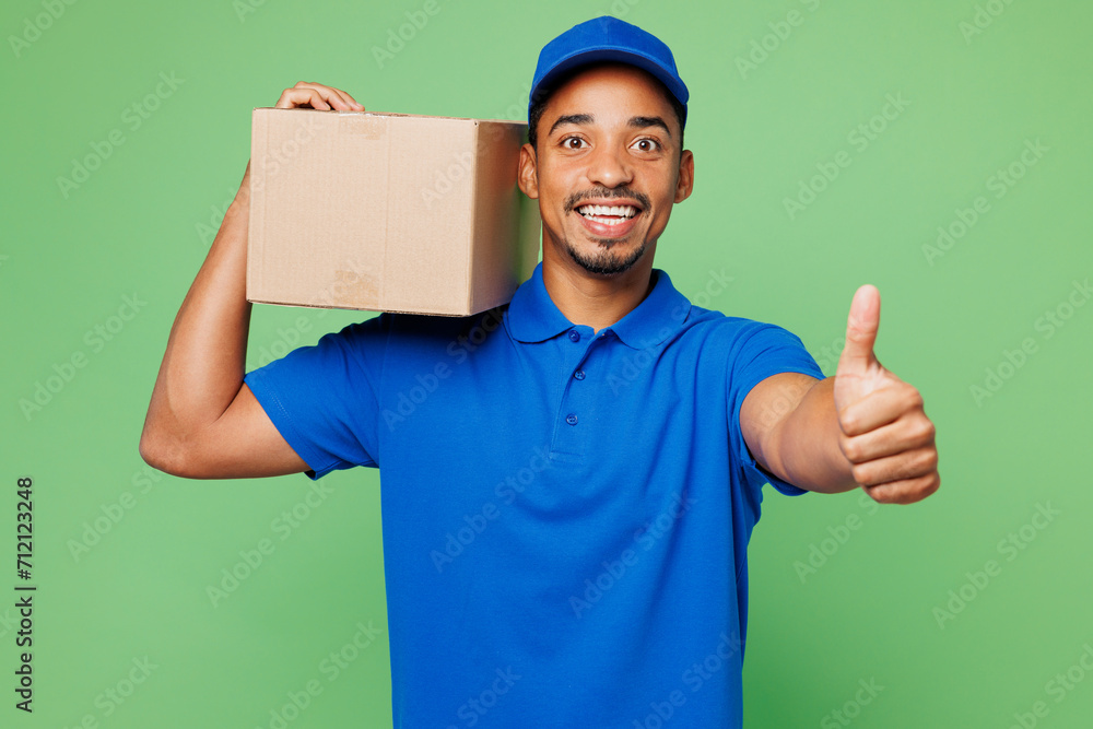 Professional fun delivery guy employee man wear blue cap t-shirt uniform workwear work as dealer courier hold blank cardboard box package show like isolated on plain green background. Service concept. Professional fun delivery guy employee man wear blue cap t-shirt uniform workwear work as dealer courier hold blank cardboard box package show like isolated on plain green background. Service concept.
