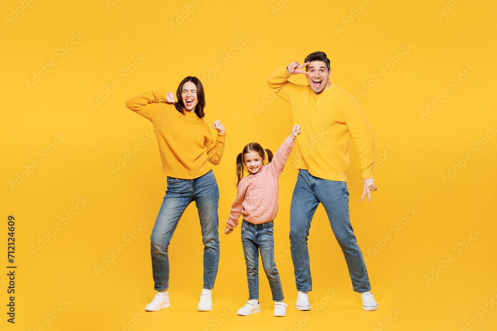 Full body young fun happy parents mom dad with child kid girl 7-8 years old wear pink sweater casual clothes do winner gesture dance show v-sign isolated on plain yellow background Family day concept