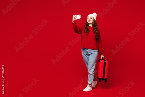 Traveler woman wear sweater hat casual clothes hold bag do selfie shot mobile cell phone isolated on plain red color background Tourist travel abroad in free time rest getaway Air flight trip concept #712124822