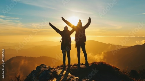 Two people silhouette with arms raised up on mountain top at sunset © MdKamrul