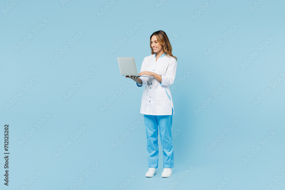 Full body female doctor woman wear white medical gown suit work in hospital clinic office hold use laptop pc computer look camera isolated on plain blue background studio Health care medicine concept Full body female doctor woman wear white medical gown suit work in hospital clinic office hold use laptop pc computer look camera isolated on plain blue background studio Health care medicine concept