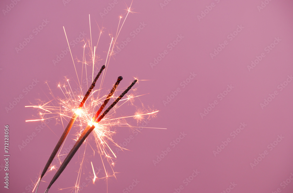 Fototapeta premium Burning sparklers burning on pink background, copy space for text.