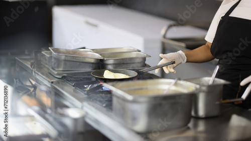 Close-up of cook prepares omelet in skillet in kitchen, cooking in cafes and restaurants. Professional chef making dessert, lunch for sale. Food concept