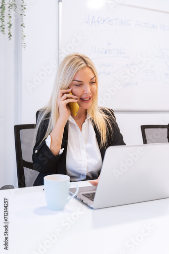 A focused businesswoman conducts a phone conversation with a marketing strategy whiteboard in the background, illustrating active corporate engagement.  © JoseIMartin