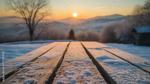The empty wooden table top with snow and frost for your decoration of product or text and landscape of winter mountains with small rural home and sunset time