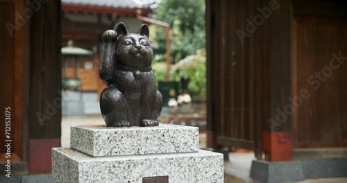 Maneki neko, statue and Japanese or traditional temple at woods garden for respect, worship or spirituality. Sculpture, lucky cat and outdoor or traveling adventure in Tokyo, Gotokuji and fortune photo