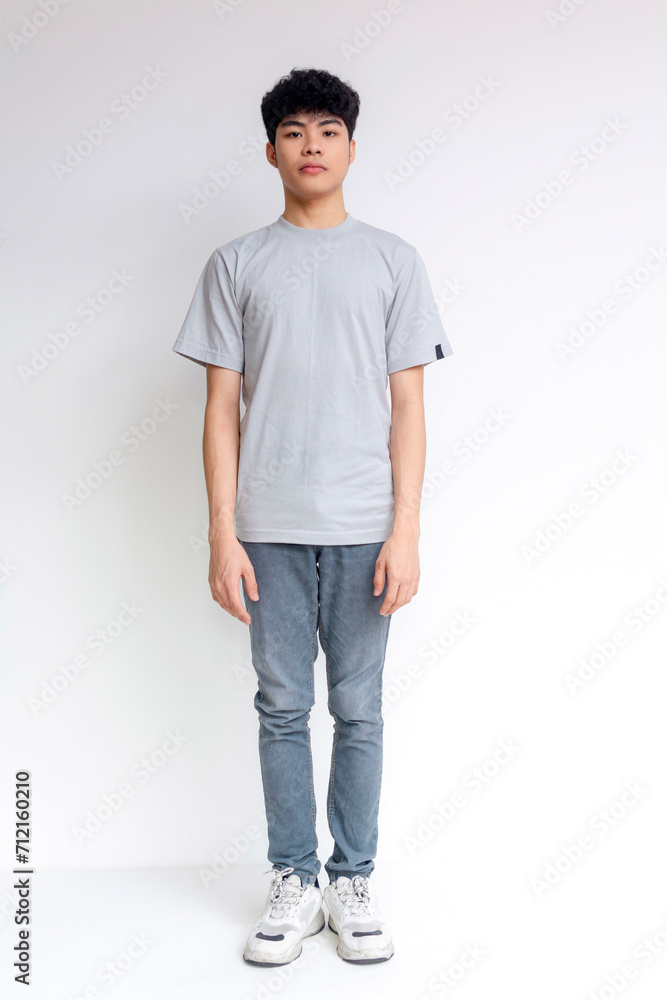 Portrait of a young man standing confidently in a grey t-shirt and jeans against a white background. Portrait of a young man standing confidently in a grey t-shirt and jeans against a white background.