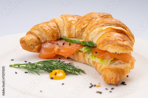 Breakfast. Croissant with salmon and vegetables on a white plate and a white background