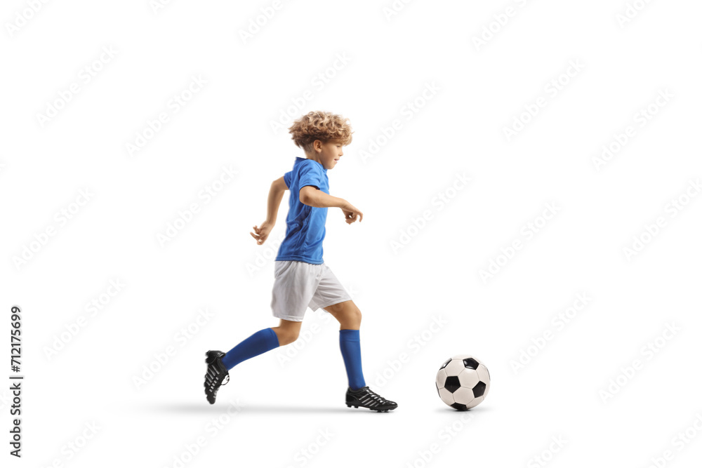 Full length profile shot of a boy in a football kit running and leading a ball